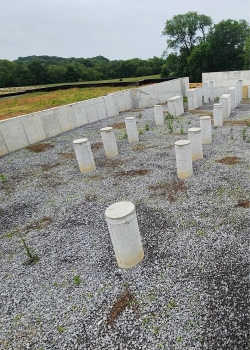 A lot of cement poles sitting on top of a gravel field